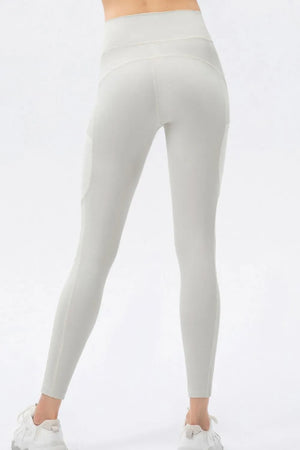 A person shown from the back wearing high-waisted seamless leggings in a light warm gray or off-white shade, paired with white sneakers, against a plain white studio background.