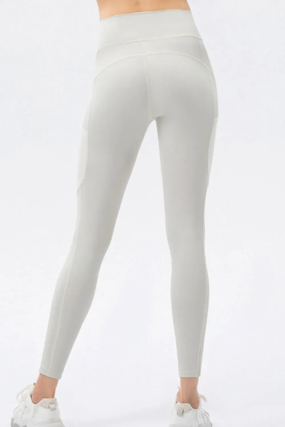 A person shown from the back wearing high-waisted seamless leggings in a light warm gray or off-white shade, paired with white sneakers, against a plain white studio background.