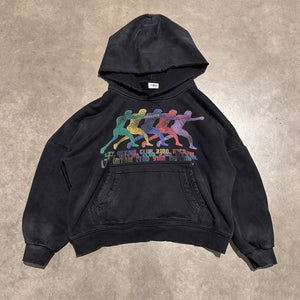 A faded black pullover hoodie laid flat on a textured concrete floor, featuring a colorful graphic of four athletes holding a chain in the center with the text 'LET'S BREATHE CLUB 2ND GENERATION' and 'OCT 1971 - OCT 2021'.
